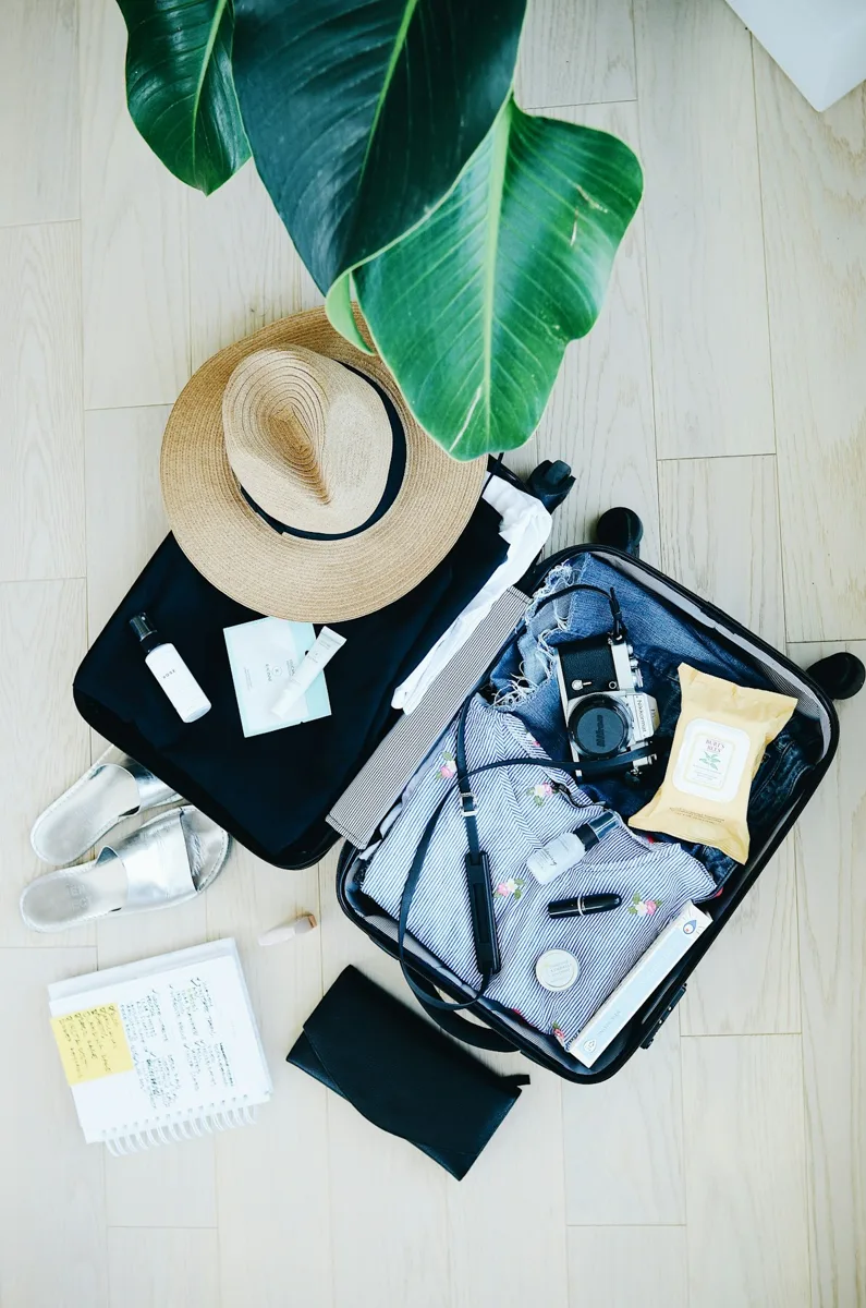 An open suitcase packed with clothes, a hat and travel accessories