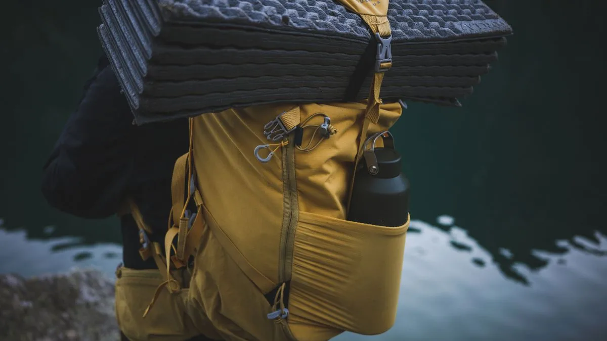 A water bottle packed with a yellow backpack beside the water